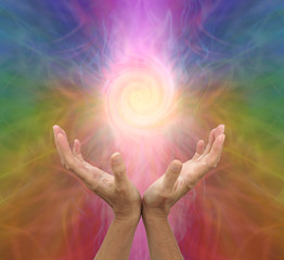 Wall Mural - Channeling rainbow coloured  vortex healing energy  - female hands held open and palms upwards with a spiraling energy formation above on a multicoloured background and copy space