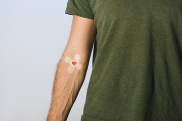 Partial view of patient in green t-shirt with plasters on grey background, blood donation concept