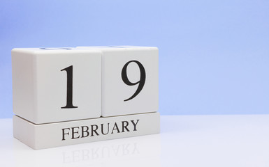 February 19st. Day 19 of month, daily calendar on white table with reflection, with light blue background. Winter time, empty space for text