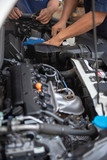Fototapeta  - Car service by an auto mechanic in garage, fixing a car battery with wrench, also checking some parts of the engine showing by selective focus.