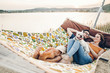 © sonyachny - Hipster family on vacation concept, happy woman and man relaxing on a hammock at the beach with their cute bulldog pet, couple lying near a lake at sunset