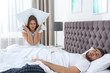 Upset young woman covering her head with pillow near sleeping husband in bedroom. Relationship problems