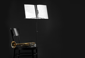 Poster - Trumpet, chair and note stand with music sheets on black background. Space for text