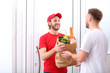 © New Africa - Courier giving paper bag with products to customer at home. Food delivery service