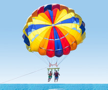 Happy Couple Parasailing In Turkey Beach In Summer. Couple Under Parachute Hanging Mid Air. Having Fun. Tropical Paradise. Positive Human Emotions, Feelings, Family, Children, Travel, Vacation.