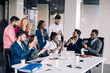 © alfa27 - Mixed-race group of nine diverse happy people standing arround the table with colleagues seated , applauding team achievements