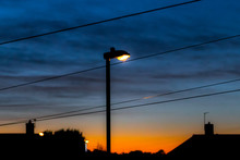 Illuminating Orange/white Street Light In Foreground With Dramatic And Moody Sky With Clouds.