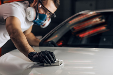 young man clears polish a vehicle. close up photo. copy space. mecchanic using sandpaper at workplace