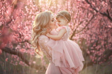 Portrait of young beautiful mother with her little girl. Close up still of loving family. Attractive woman holding her child in pink flowers and smiling