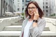 Business communication. Young lady in eyeglasses standing on the city street talking on smartphone joyful close-up