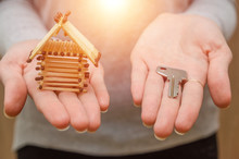 The Girl Is Holding A Small House Of Matches And A Key On The Palms. Concept Housing Construction. Photo With Flare