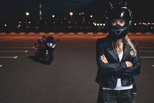 Picture Of Confident Self Determined Young Female Rider In Safety Helmet Standing In Parking Lot Keeping Arms Crossed And Looking At Camera, Going To Have Ride On Motorcycle Around Night City