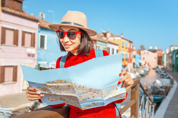 Wall Mural - Young female traveler with hat looking at the map on the bridge on Burano island, Venice
