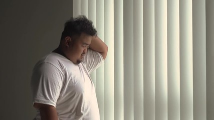 Wall Mural - Frustrated overweight man standing near the window while thinking and scratching his head. Shot in 4k resolution