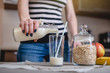© Artem - Woman pours organic oat milk from a bottle into a glass on a table in the kitchen. Diet healthy vegetarian product