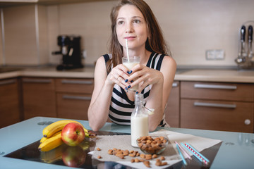 Woman drinking organic almond milk holding a glass in her hand in the kitchen. Diet vegetarian product