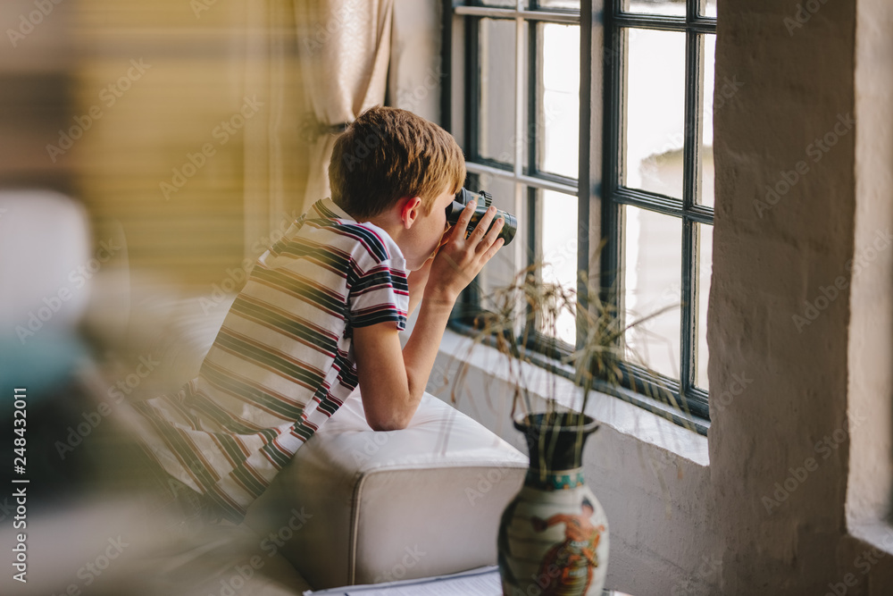 Curious boy looking out the window with binocular