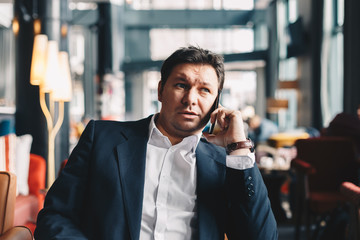 Handsome young businessman in his thirties sitting in a cafe bar during a break from work, talking finance by using a mobile phone. Concept of working on a break.