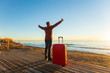 © satura_ - Trip, travel, summer and holidays concept - Happy man with red case is standing on a beach and watching a sunset