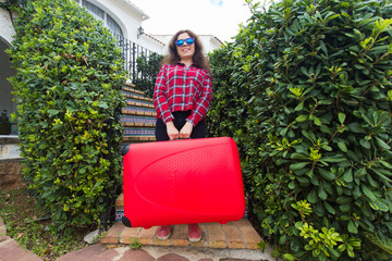 Wall Mural - Holiday, travel and tourism concept - surprised young woman with heavy red suitcase