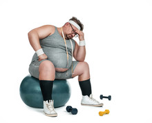 Funny Overweight Sports Man Sitting Depressed On The Fitness Ball Isolated On White Background