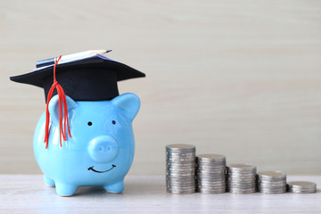 Graduation hat on blue piggy bank with stack of coins money on wooden background, Saving money for education concept