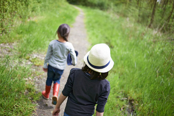 Two cute young Asian girls enjoying walking in high grass surrounded by nature in spring sunshine