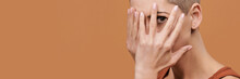 Beautiful Young Woman With Shaved Head Covering Her Face With Both Hands And Peeking Through Fingers. Woman With Frightened Expression Isolated Over Brown Background.