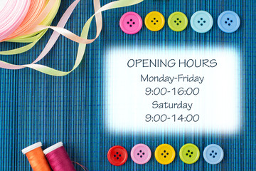 Opening hours sign of tailoring shop: two rows of colorful buttons, threads and ribbons on a dark blue straw mat - white rectangular text space