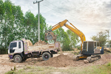 Wall Mural - Yellow excavator machine loading soil into a dump truck at construction site