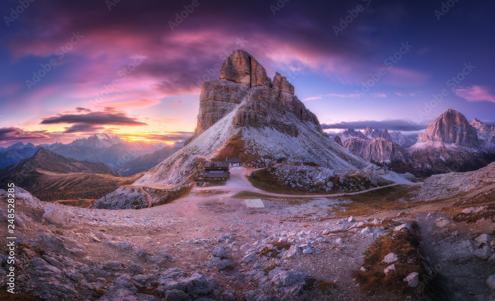 Mountain pass and beautiful sky with colorful clouds at sunset. Amazing panoramic landscape with rocks, mountain peaks, stones, trails, buildings, trees on hills at dusk. Autumn in Dolomites, Italy - obrazy, fototapety, plakaty 