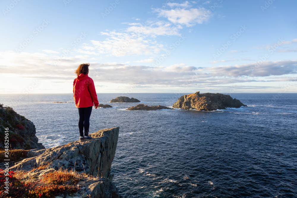 Woman in red jacket is standing at the edge of a cliff and enjoying the ...