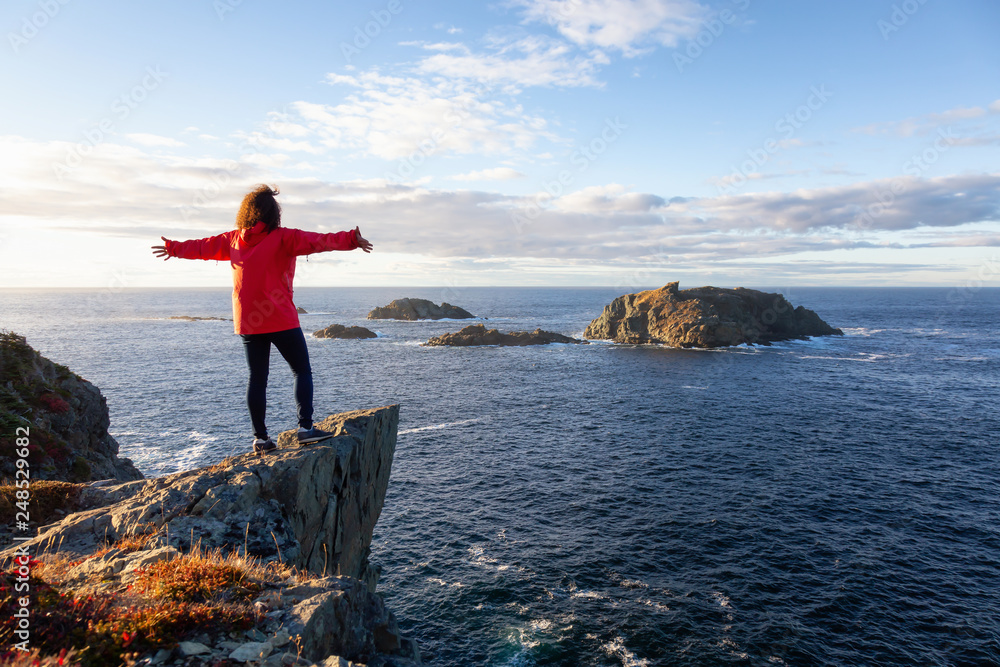Woman in red jacket is standing at the edge of a cliff with open arms ...