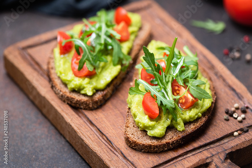 Fotografía Healthy vegan toast with avocado, tomato, arugula on wooden serving board, closeup view, horizontal image