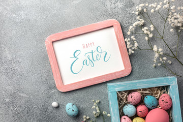 Colorful easter eggs in box and flowers on table. Top view with copy space.