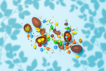 Wall Mural - Broken and whole chocolate Easter eggs, multicolored sweets on blue background. Concept of celebrating Easter, Easter decorations, search for sweets for Easter Bunny. Flat lay, top view. Copy Space