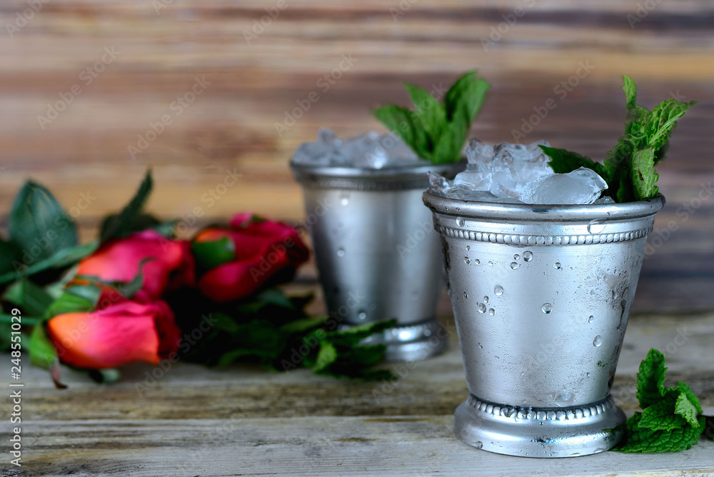 Image for Kentucky Derby in May showing two silver mint julep cups with crushed ice and fresh mint in a rustic setting with red roses - obrazy, fototapety, plakaty 
