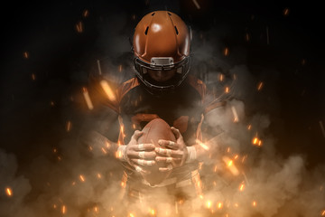 American football player on dark background in smoke and sparks in black and orange outfit.