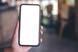 © Farknot Architect - Mockup image of a hand holding and showing black mobile phone with blank white screen in modern cafe
