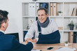 worker in neck brace with broken arm and businessman in blue jacket shaking hands over table in office, compensation concept