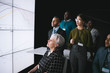 © JonoErasmus - Business group having a discussion during a conference, looking a large video wall with charts and graphs