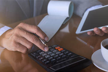 Wall Mural - Man hand  holding digital tablet and using calculator to calculate business budget with checkbook on the desk at office. Business plan and paycheck concept.