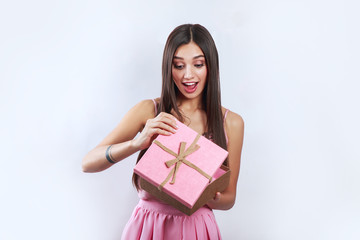 Portrait of a happy smiling brunette girl opening a pink gift box isolated over gray background