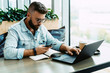 © foxyburrow - Hipster man sits in cafe, uses smartphone, works on laptop. Businessman reads an information message in phone.