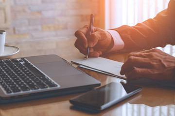 Business man hand writing and signing cheque book with laptop computer on the wooden table at modern home office. 