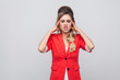 © khosrork - Portrait of sick beautiful business lady with hairstyle and makeup in red fancy blazer standing, holding her head and feeling headache.