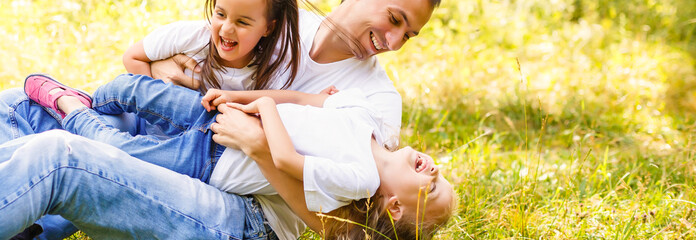 Father withHappy young family with two children outdoors two daughters in white T-shirts sitting and playing on the grass in the park