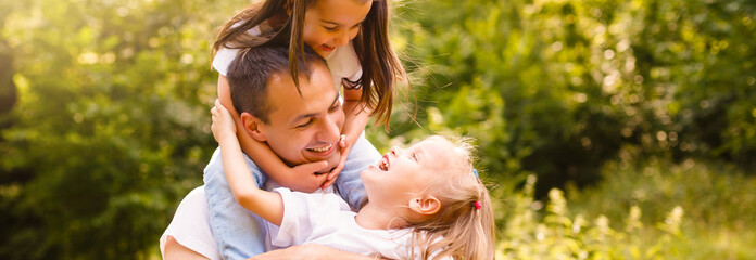 Happy father and little daughters spending time. Father and daughters playing . Little girl sitting on fathers shoulder.