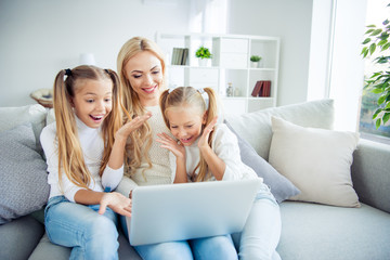 Canvas Print - Portrait of three nice-looking cute lovely attractive cheerful cheery positive people pre-teen girls mom sitting on divan making video call w-fi in light white interior room indoors