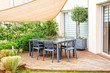 Modern outdoor wooden terrace with dining table, chairs and a shade sail